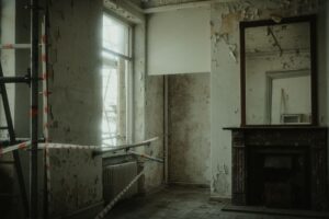 Abandoned room with peeling walls, construction tape, and a large mirror creating a creepy atmosphere.