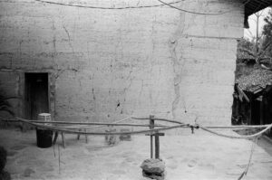 Black and white photo of a rustic adobe house with visible ropes and texture.