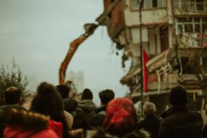 A crowd observes a building being demolished in a cold urban setting.