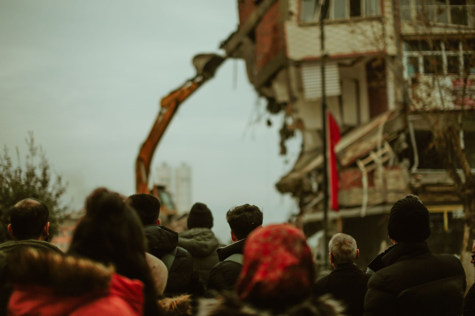 A crowd observes a building being demolished in a cold urban setting.