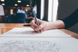 A person focuses on writing or sketching in a creative workspace setting.