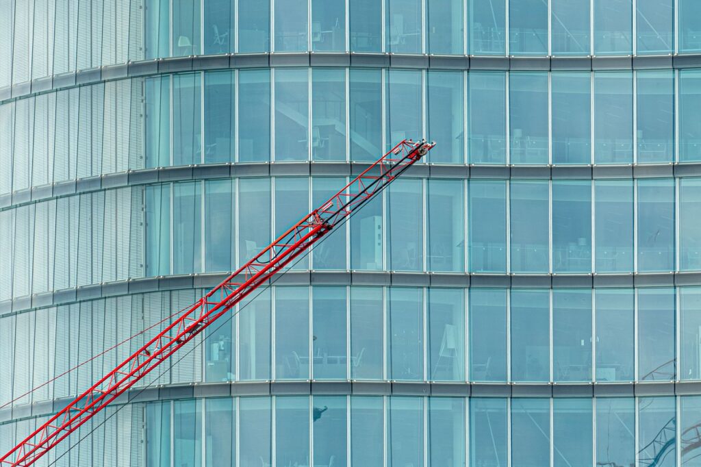 Close-up of a modern glass building facade with a red crane in the foreground.