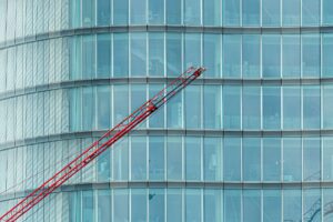 Close-up of a modern glass building facade with a red crane in the foreground.