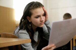 Young woman in a classroom deeply focused on reading a document, holding her head thoughtfully.