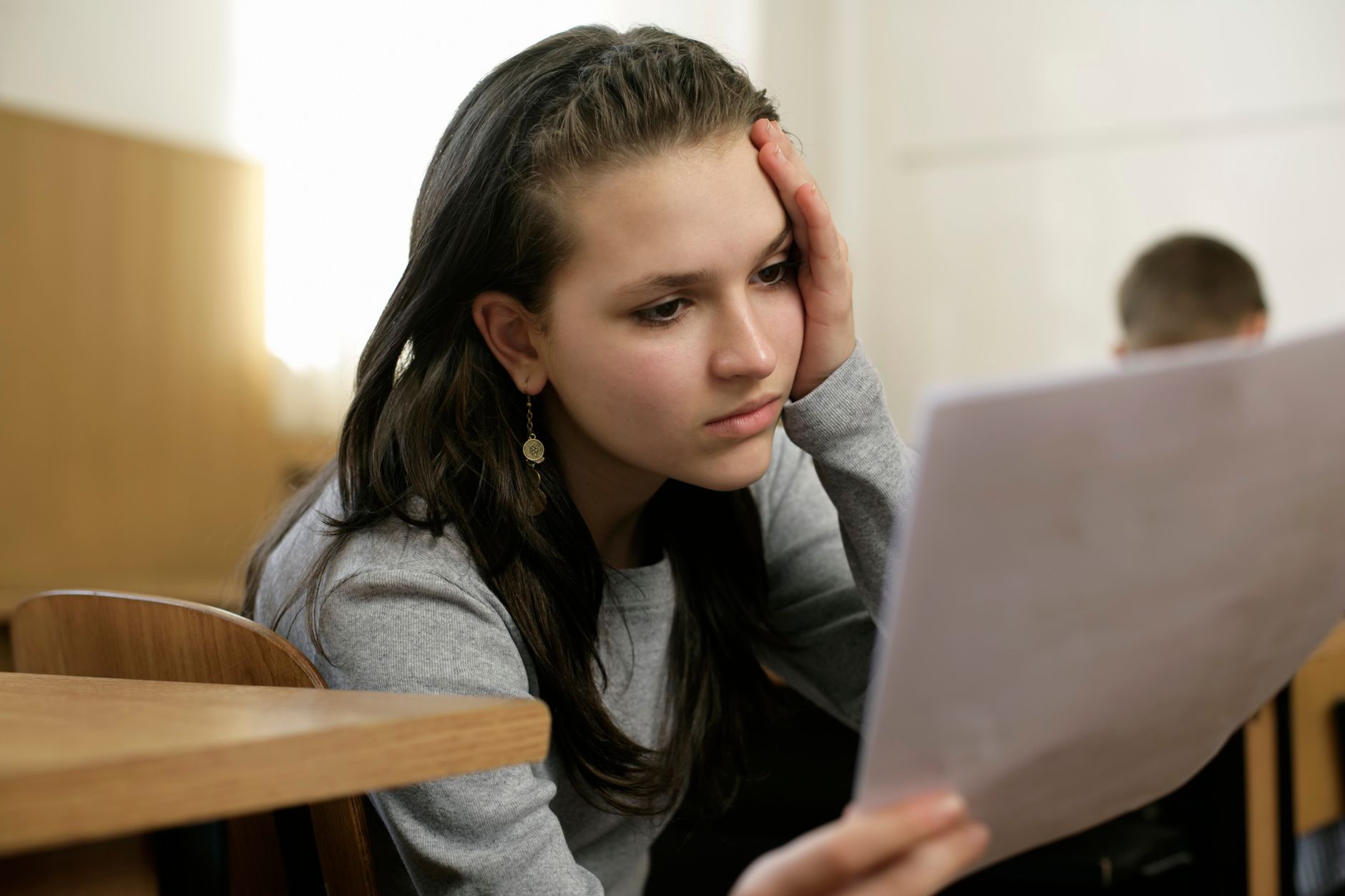 Young woman in a classroom deeply focused on reading a document, holding her head thoughtfully.
