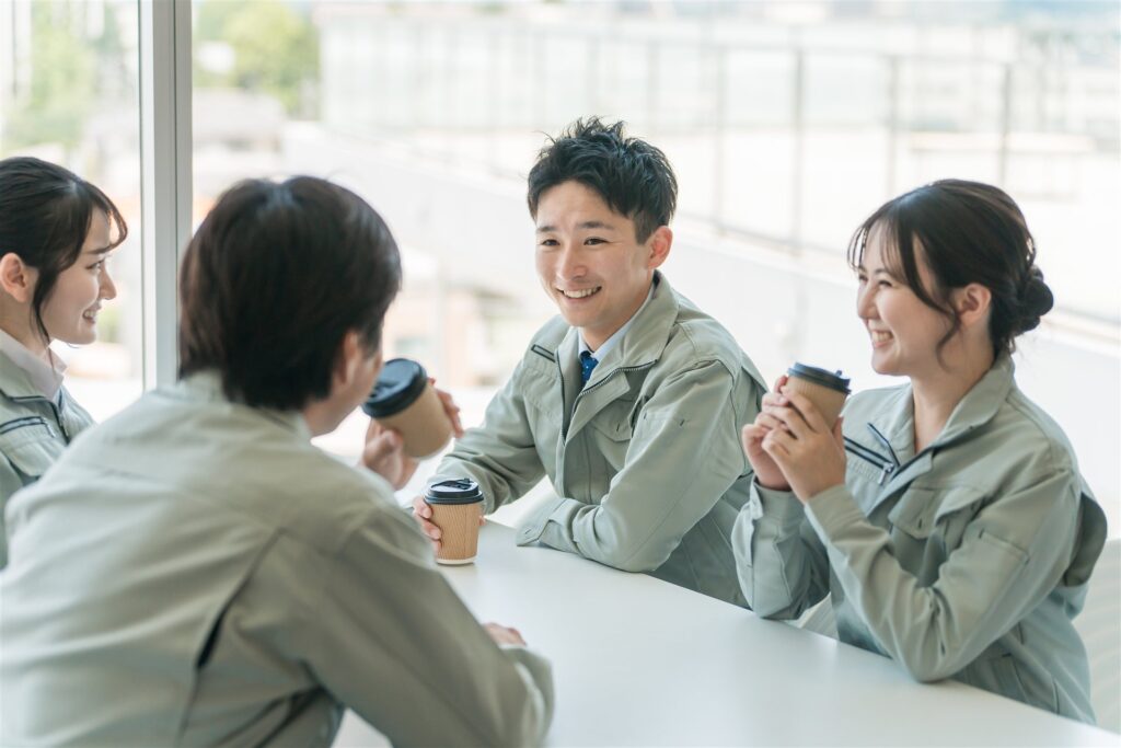 休憩室で飲み物を手に談笑する作業服の男女