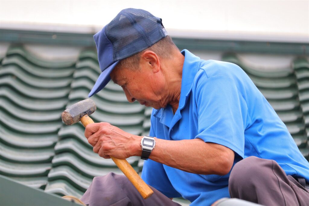 屋根の上で金づちを持って作業する年配の職人