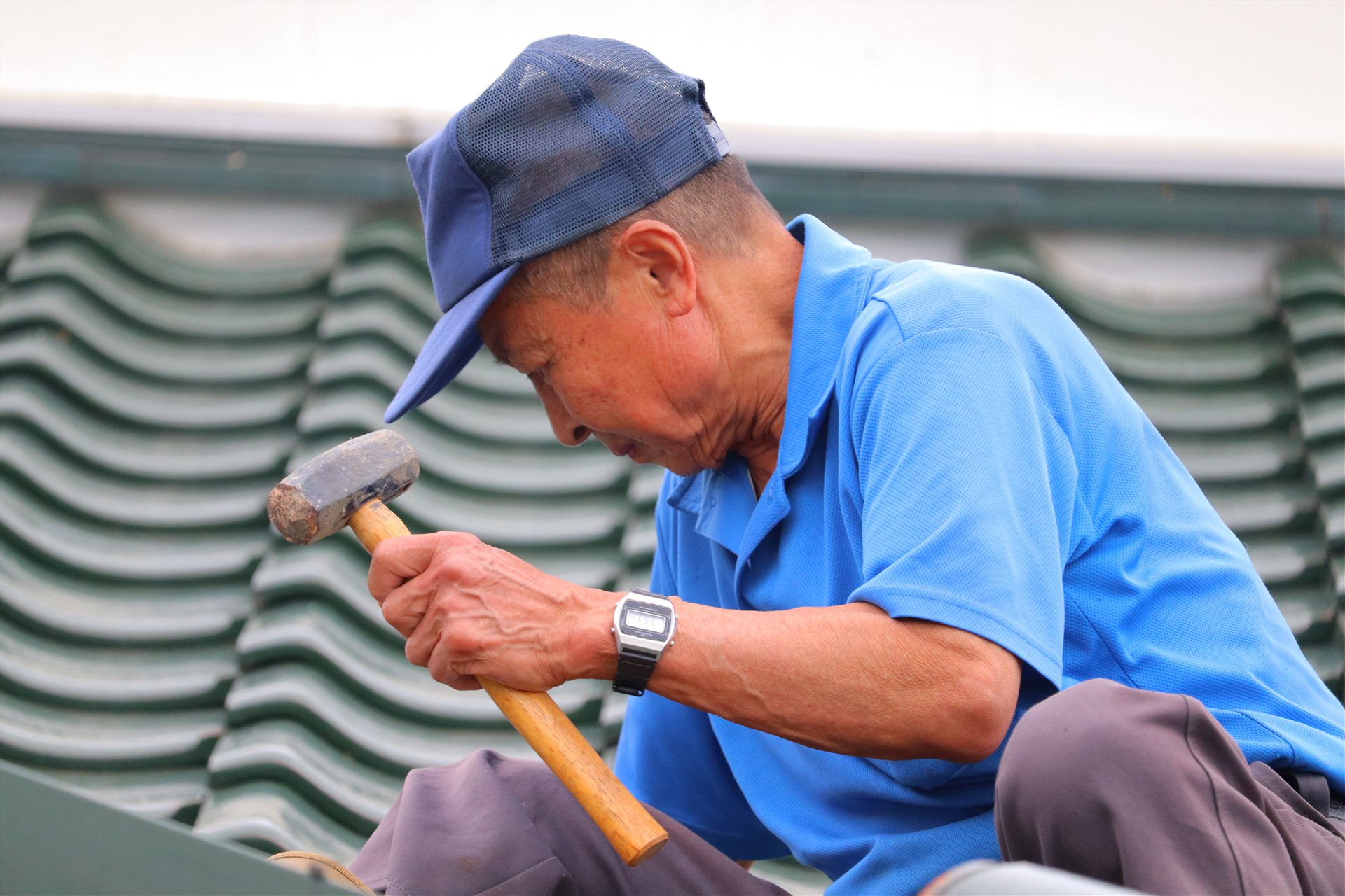 屋根の上で金づちを持って作業する年配の職人
