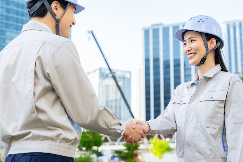 建設現場で握手する作業着とヘルメットの男女
