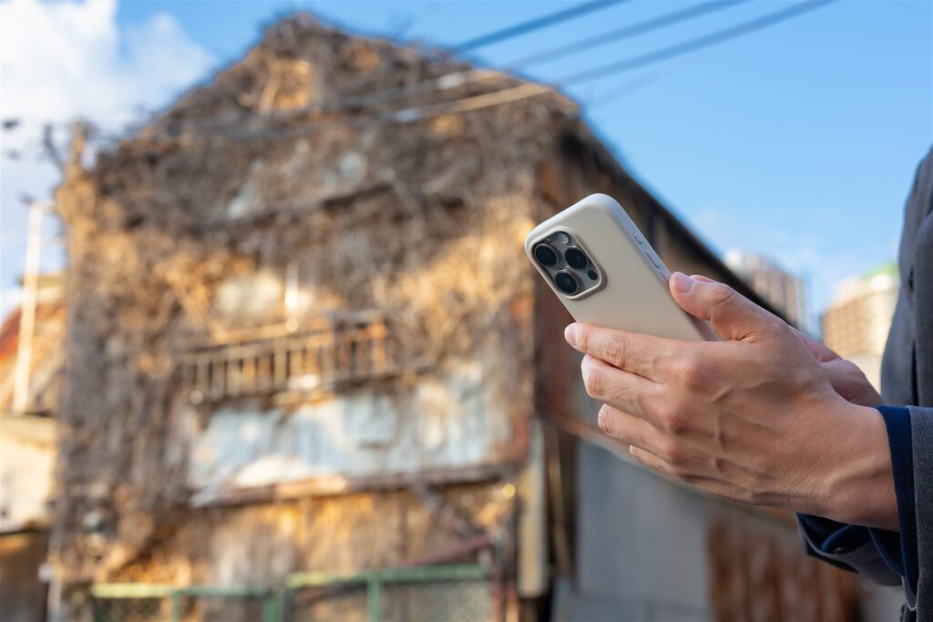 つたの絡んだ古い家の前でスマートフォンを構える手