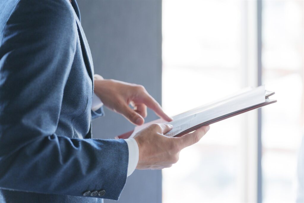 スーツの人がファイルの書類を指でたどる手元