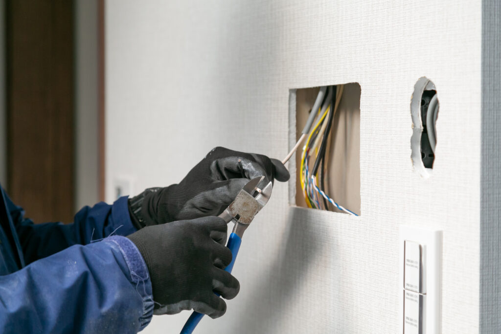 壁の穴から出た電線をニッパーで切る手元