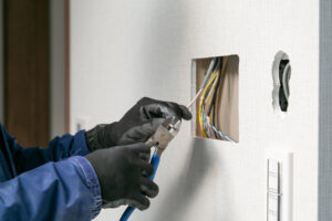 壁の穴から出た電線をニッパーで切る手元