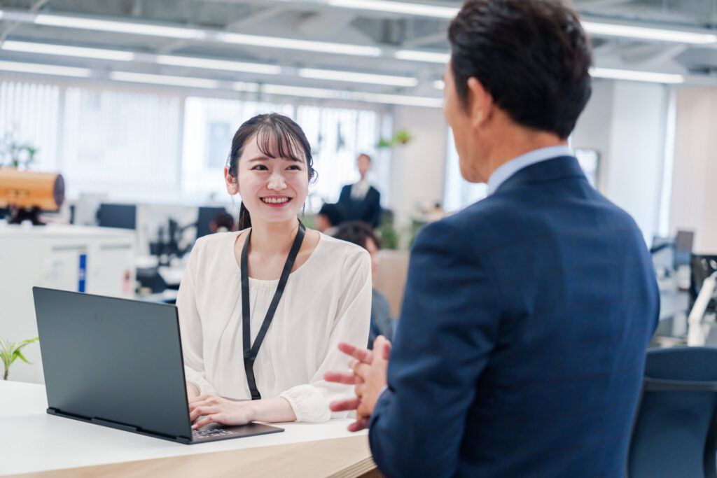事務所の受付で来訪の男性に対応する名札の女性