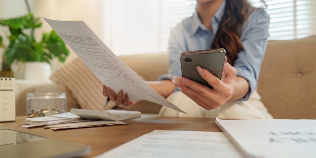 ソファで書類を手に持ちスマホと見比べる女性