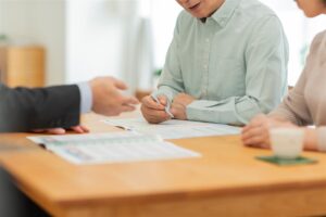 机で書類を見る夫婦とスーツの担当者の手元