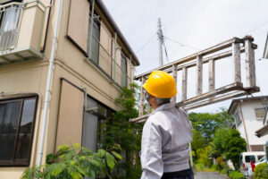 2階建ての家の前で脚立をかついだ作業員
