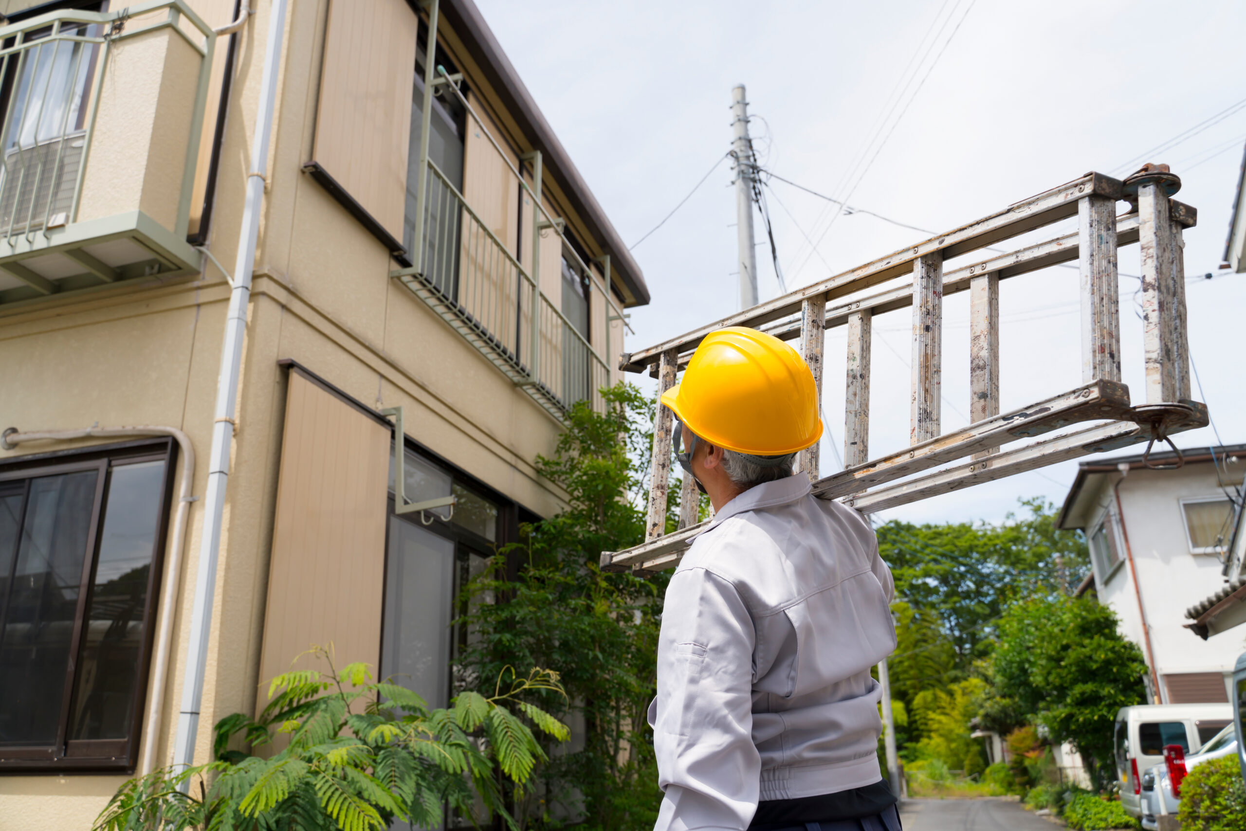 2階建ての家の前で脚立をかついだ作業員