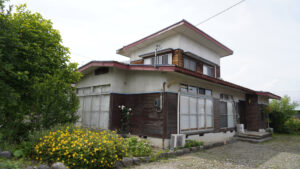 庭に花が咲く古い2階建ての住宅の外観