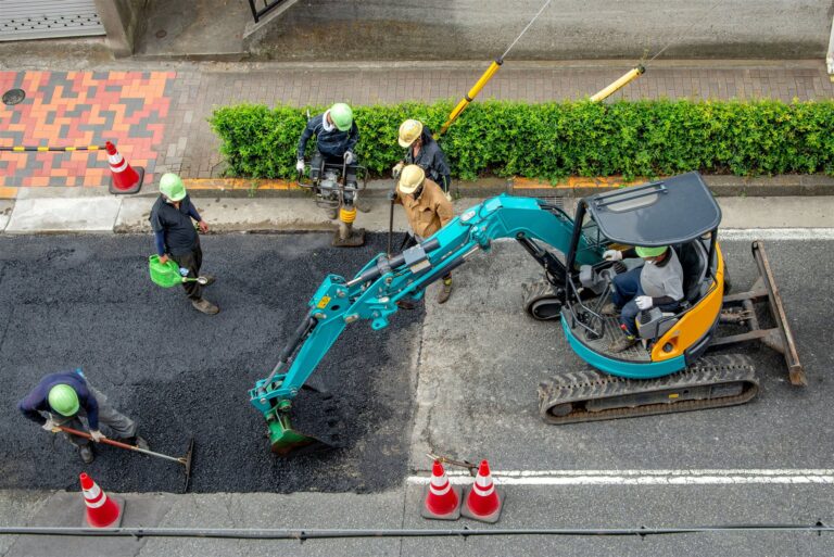 アスファルトの道路を直す作業員と小型ショベル
