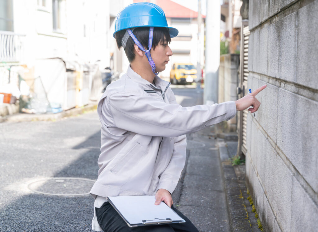 住宅地のブロック塀を指さして確かめる作業員