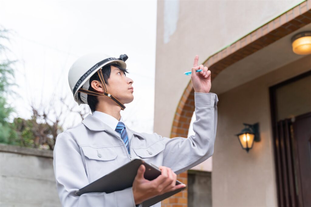 住宅の玄関の外でバインダーを持ち上を指して見上げる作業員