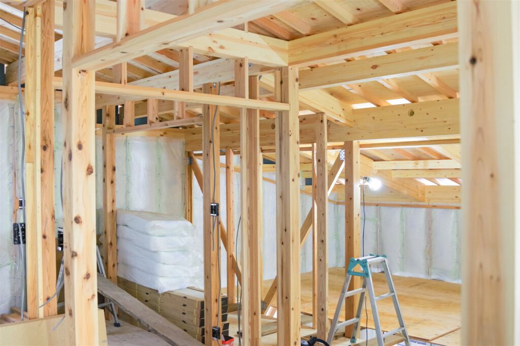 柱と梁が並ぶ建築中の木造住宅の室内と断熱材の束