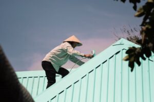 笠をかぶって屋根を塗装する作業員