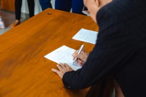 木の机で書類に署名するスーツ姿の男性