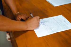 木の机で書類に署名する人の手元