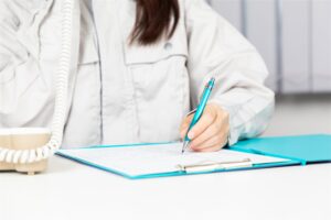 作業着の人がバインダーの書類に書き込む手元と電話