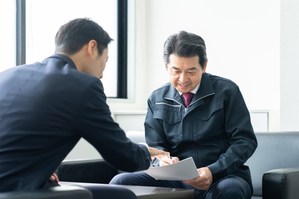 作業着の男性と書類を見て相談する人