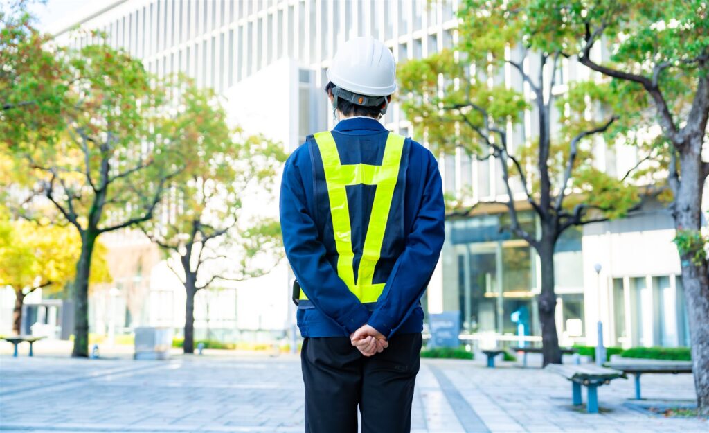 ビルの前に立つ反射ベストとヘルメットの作業員の後ろ姿