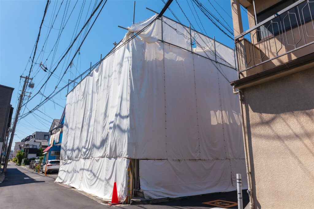白いシートで覆われた解体中の建物と電線
