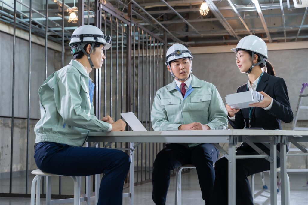 建築現場の机で打ち合わせる作業員と担当者