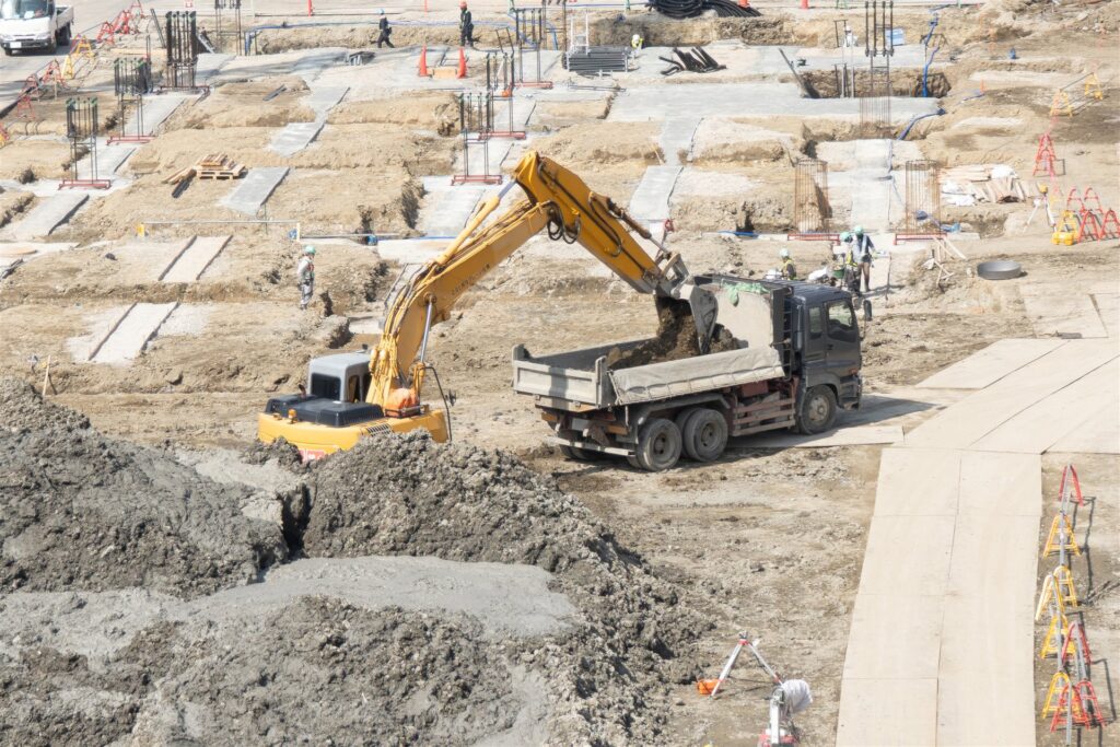 基礎工事の現場で油圧ショベルがダンプに土を積み込む様子