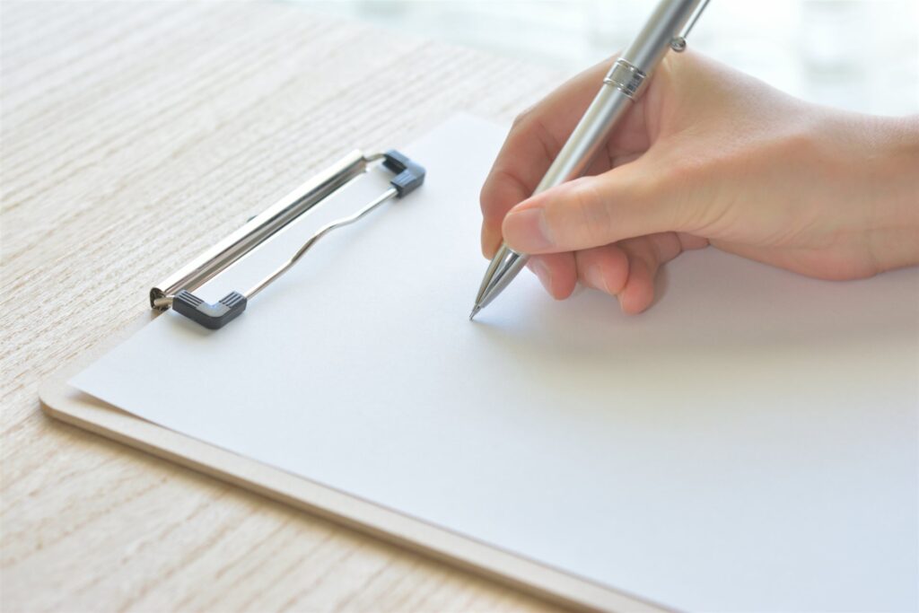 クリップボードの白い紙にペンで書く手元