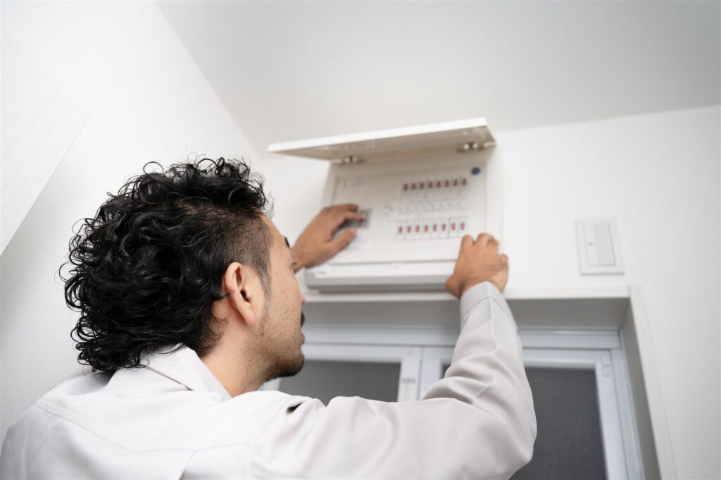 作業員が壁の分電盤のふたを開けて作業する