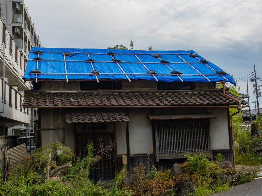 瓦屋根にブルーシートを張り土のうで押さえた木造の住宅