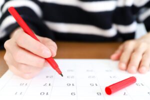 カレンダーに赤いペンで書き込む手元