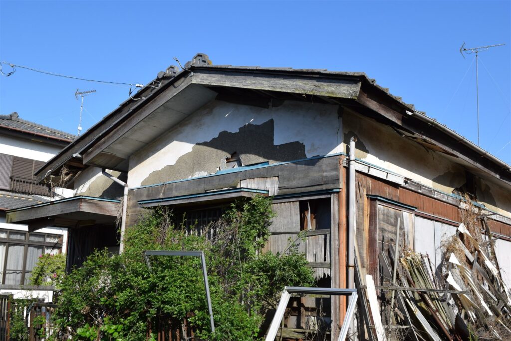 壁の塗りがはがれ板が崩れかけた古い木造の空き家