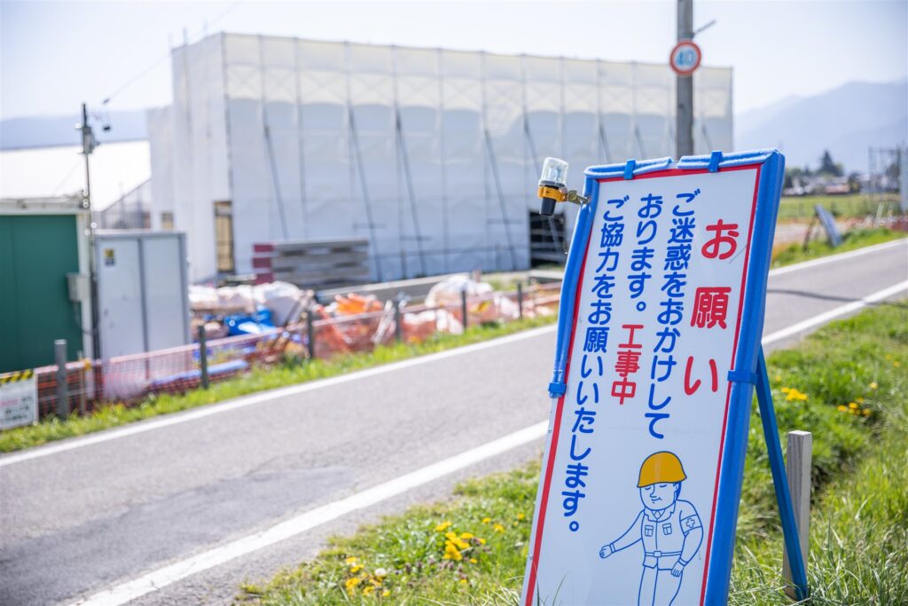 道路わきの工事中のお願いの看板と白いシートで囲った建物