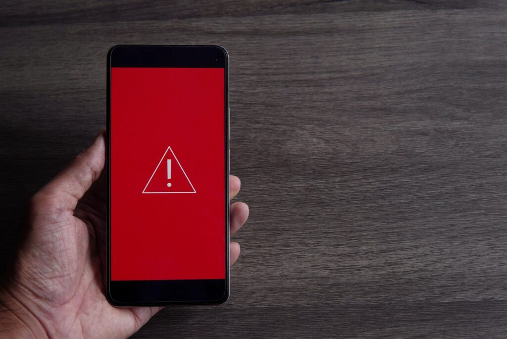 赤い画面に警告の印が出たスマートフォンを持つ手