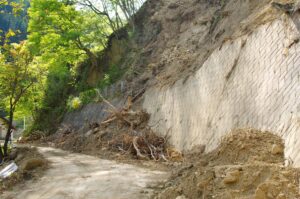 崩れた斜面の土砂と木の根がブロックの擁壁の前にたまった道