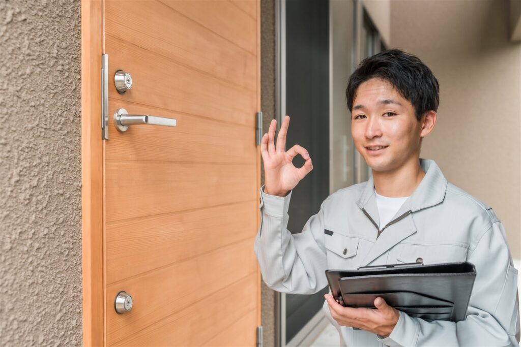 玄関の前で板を持ち手で丸の合図をする作業着の人