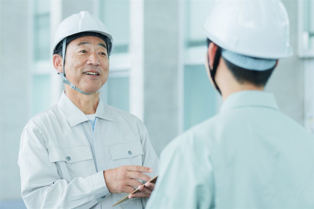 ヘルメット姿の年配の作業員と若い作業員の打ち合わせ